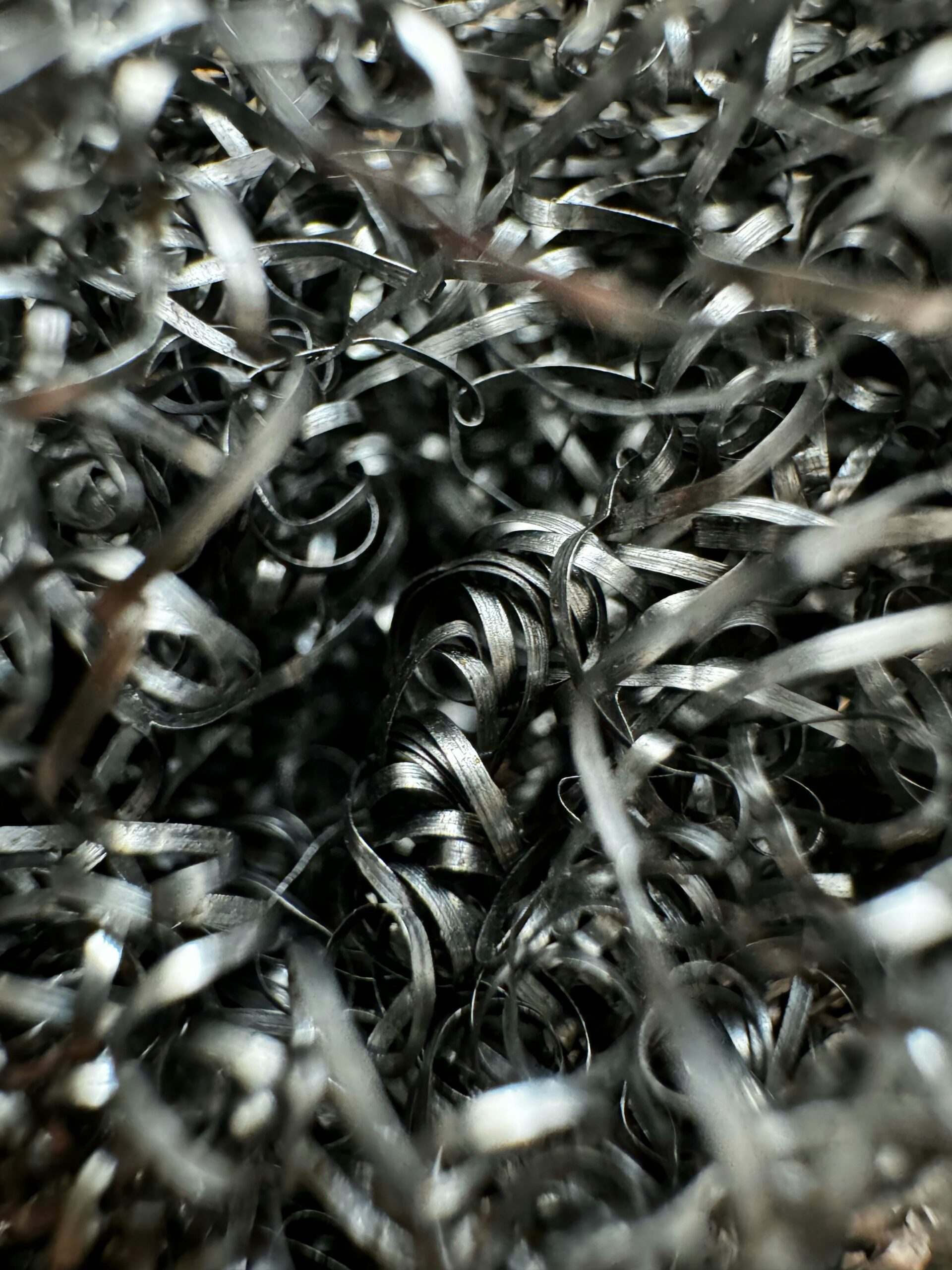 Close-up image of tangled, curly metal shavings with a shiny silver appearance, creating an abstract and chaotic texture.